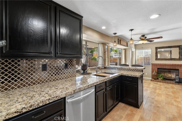 kitchen featuring dark cabinetry, a fireplace, a sink, dishwasher, and tasteful backsplash