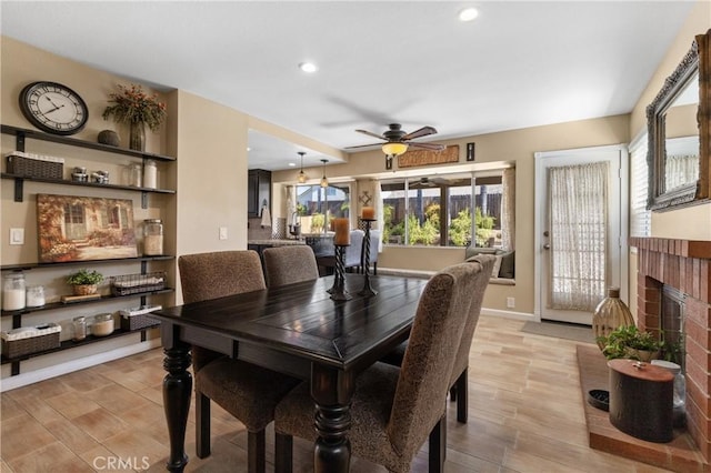 dining room with a ceiling fan, baseboards, light wood finished floors, a fireplace, and recessed lighting