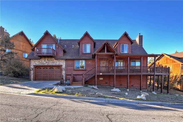 view of front of home with driveway, faux log siding, a garage, a balcony, and a chimney