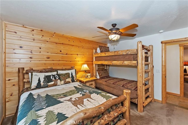 bedroom featuring wood walls, a textured ceiling, a ceiling fan, and baseboards