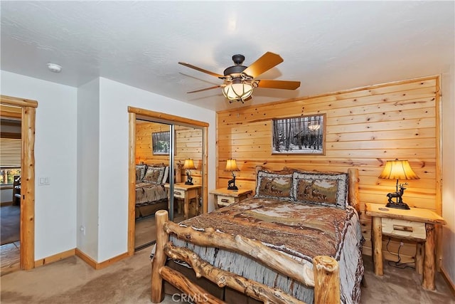 bedroom with a closet, wooden walls, baseboards, light colored carpet, and ceiling fan