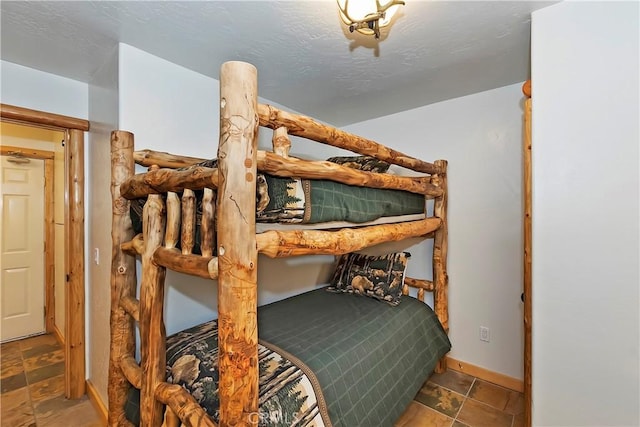 bedroom with stone finish flooring, baseboards, and a textured ceiling