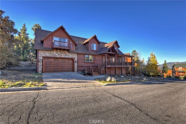 view of front of property with a balcony, driveway, an attached garage, stone siding, and faux log siding