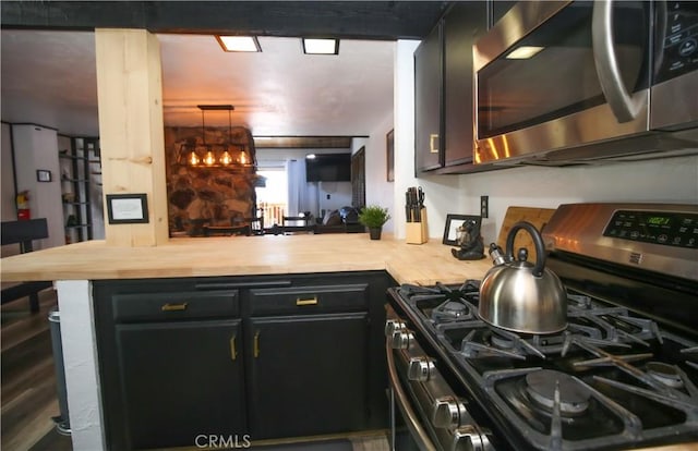 kitchen with appliances with stainless steel finishes, butcher block counters, and a peninsula