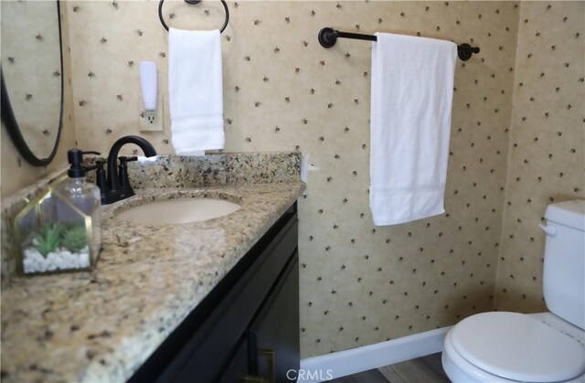 bathroom featuring toilet, wallpapered walls, vanity, and baseboards