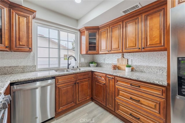 kitchen featuring visible vents, backsplash, appliances with stainless steel finishes, brown cabinetry, and a sink