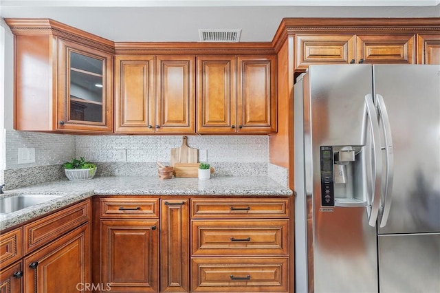 kitchen featuring visible vents, stainless steel fridge with ice dispenser, glass insert cabinets, brown cabinets, and backsplash