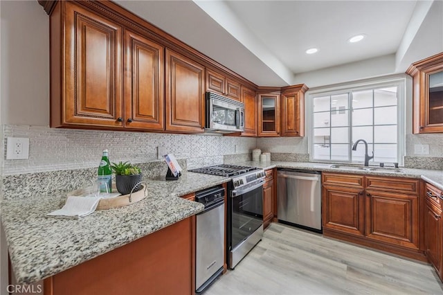 kitchen with light stone countertops, brown cabinets, appliances with stainless steel finishes, light wood-style floors, and a sink