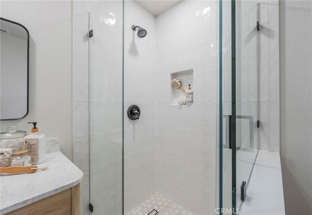 bathroom featuring vanity, a textured wall, and tiled shower