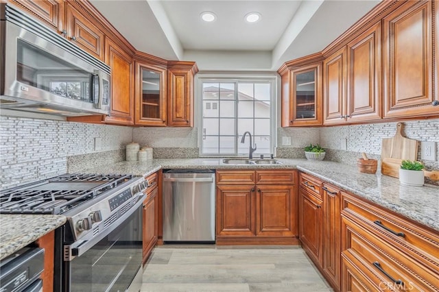 kitchen with brown cabinetry, appliances with stainless steel finishes, light stone counters, and a sink