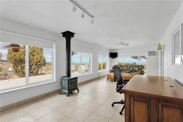 office featuring baseboards, ceiling fan, a wall mounted air conditioner, a wood stove, and light tile patterned flooring