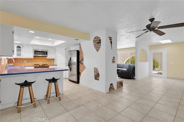 kitchen with a sink, tasteful backsplash, appliances with stainless steel finishes, a peninsula, and a raised ceiling