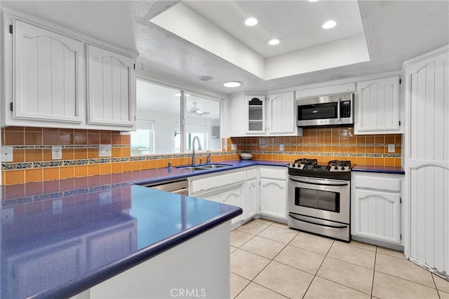 kitchen with dark countertops, a sink, stainless steel appliances, white cabinetry, and a raised ceiling