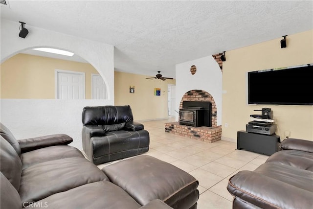 living area with light tile patterned floors, a ceiling fan, baseboards, a wood stove, and a textured ceiling