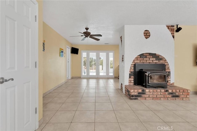 unfurnished living room with ceiling fan, light tile patterned floors, french doors, a wood stove, and a textured ceiling