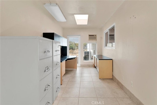 kitchen featuring dark countertops, baseboards, a wall mounted air conditioner, light tile patterned floors, and a skylight