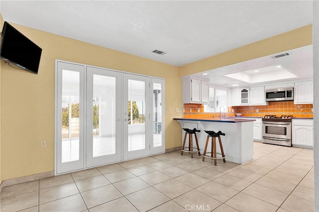 kitchen featuring a tray ceiling, stainless steel appliances, a breakfast bar area, white cabinets, and decorative backsplash