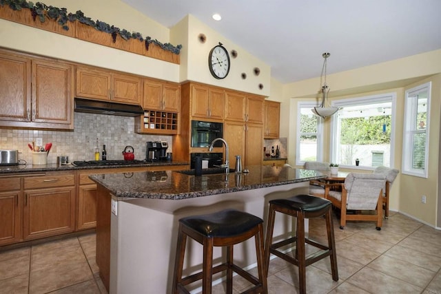 kitchen featuring under cabinet range hood, decorative backsplash, gas cooktop, and brown cabinetry