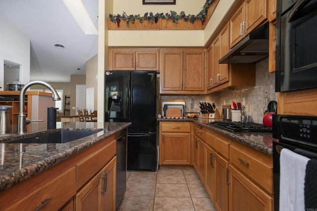 kitchen with brown cabinets, black appliances, under cabinet range hood, a sink, and light tile patterned flooring