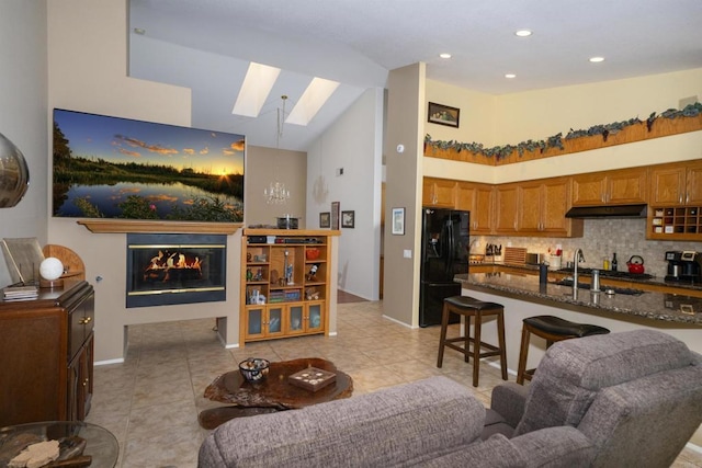 living room featuring recessed lighting, a skylight, light tile patterned flooring, a glass covered fireplace, and high vaulted ceiling