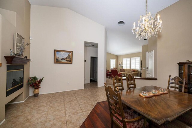 dining room featuring tile patterned floors, a chandelier, lofted ceiling, and a glass covered fireplace