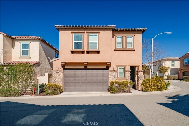 mediterranean / spanish-style home with stucco siding, stone siding, a garage, and a tile roof