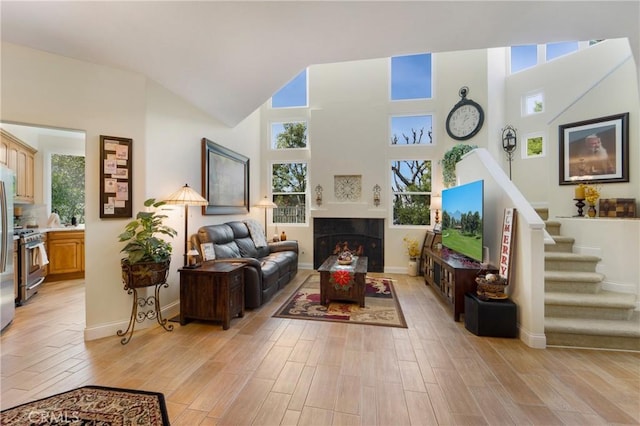 living room with stairs, high vaulted ceiling, light wood-style floors, and a fireplace