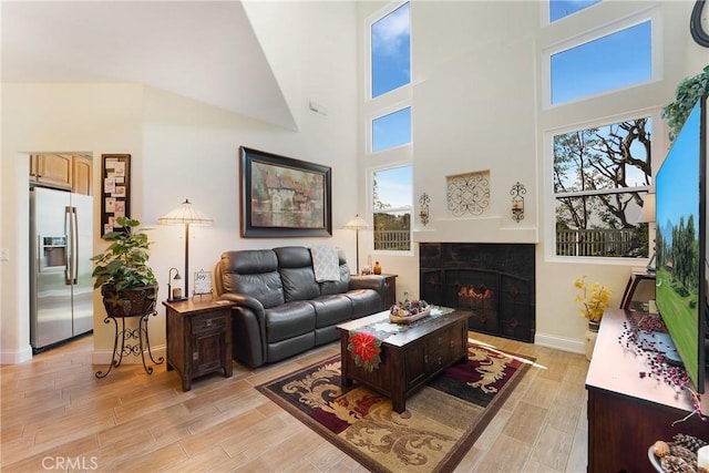 living room featuring plenty of natural light, light wood-style floors, a high ceiling, and a tile fireplace