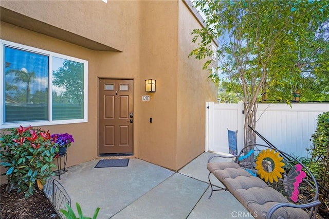 view of exterior entry with stucco siding and fence