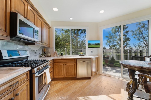 kitchen featuring tasteful backsplash, brown cabinets, appliances with stainless steel finishes, light wood-style flooring, and a sink