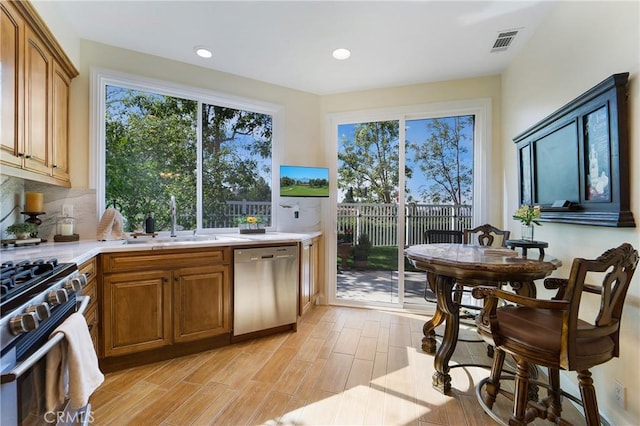 kitchen with light wood finished floors, a sink, light countertops, appliances with stainless steel finishes, and backsplash