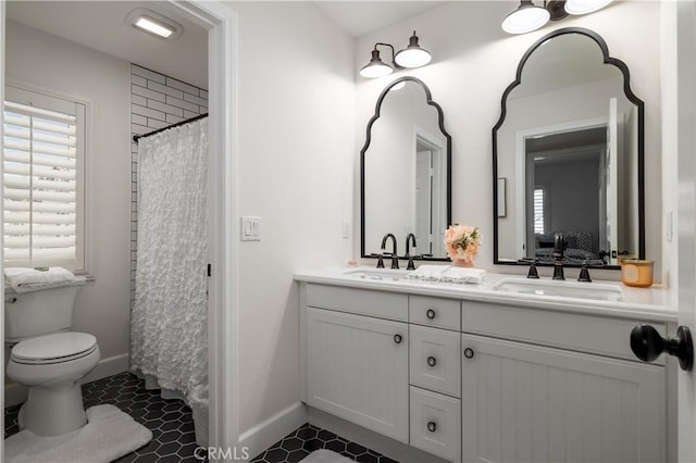 ensuite bathroom featuring double vanity, toilet, baseboards, and a sink