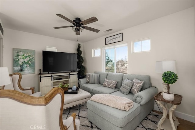 living room with visible vents, baseboards, wood finished floors, and a ceiling fan