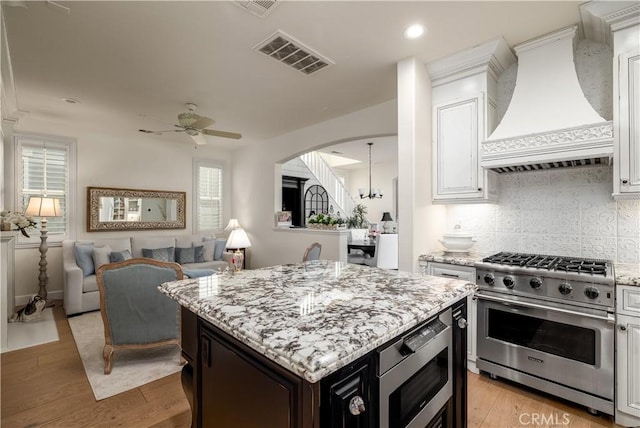 kitchen with premium range hood, visible vents, stainless steel appliances, light wood finished floors, and light stone countertops