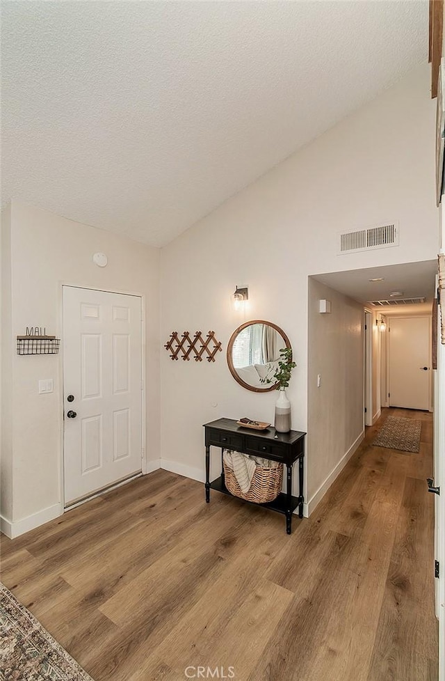 entrance foyer with visible vents, light wood-style flooring, a textured ceiling, and vaulted ceiling