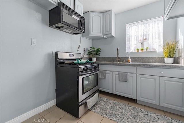 kitchen with light tile patterned floors, gas stove, a sink, white cabinets, and black microwave