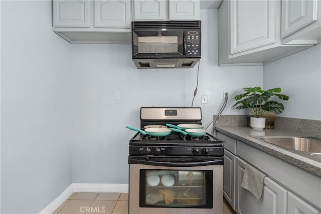 kitchen with gas stove, baseboards, light tile patterned flooring, black microwave, and white cabinetry