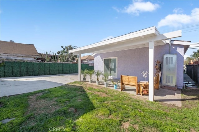 rear view of property with a yard, a patio area, fence private yard, and stucco siding