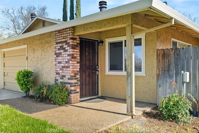 property entrance with an attached garage, fence, brick siding, and stucco siding