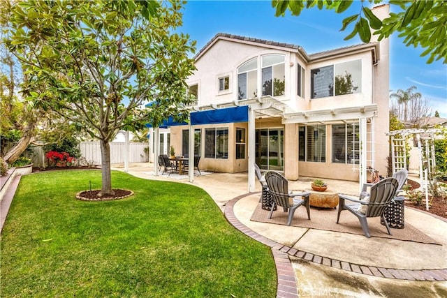 rear view of house with stucco siding, fence, a lawn, and a patio area