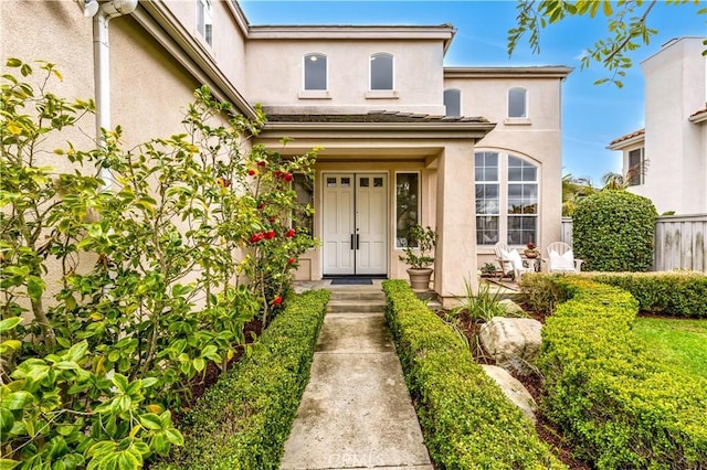 doorway to property featuring stucco siding and fence