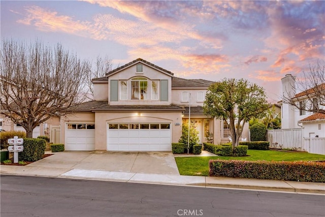 view of front facade featuring an attached garage, fence, a tile roof, stucco siding, and driveway