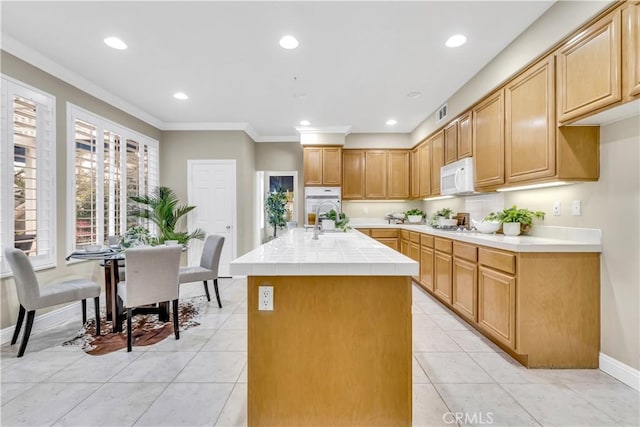 kitchen featuring crown molding, tile counters, a center island with sink, recessed lighting, and white appliances