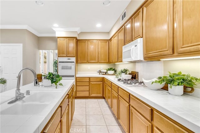 kitchen featuring white appliances, light tile patterned floors, visible vents, a sink, and tile counters