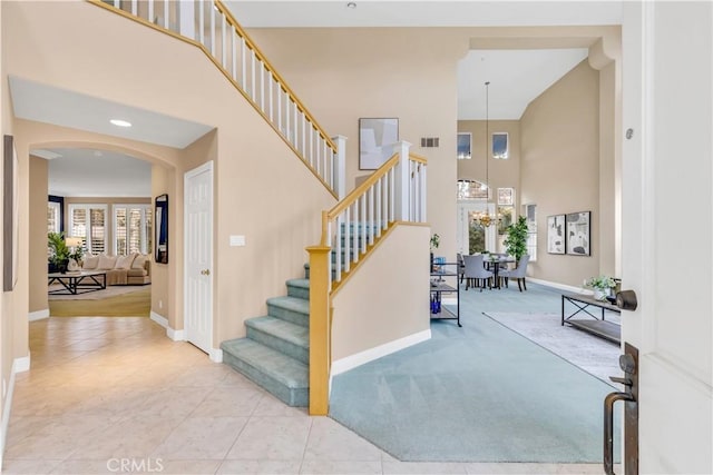 staircase featuring visible vents, baseboards, arched walkways, a towering ceiling, and tile patterned floors