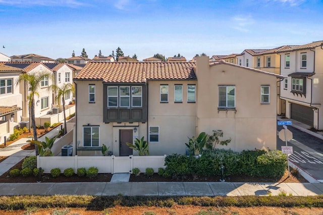 view of front of home featuring stucco siding, a tile roof, a fenced front yard, central AC, and a residential view