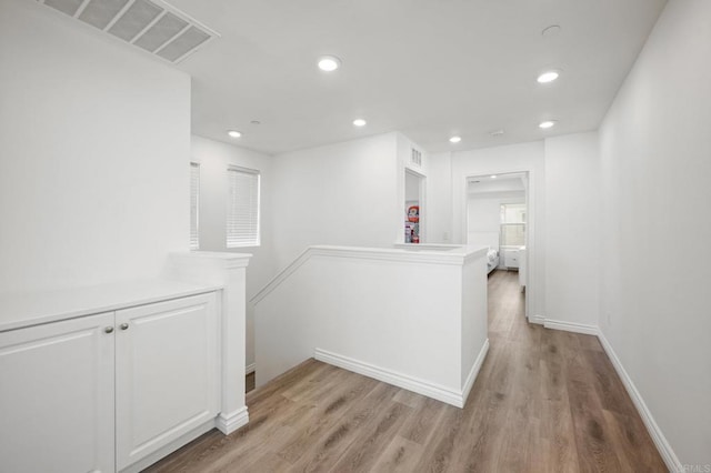 hallway featuring light wood-type flooring, visible vents, baseboards, and recessed lighting