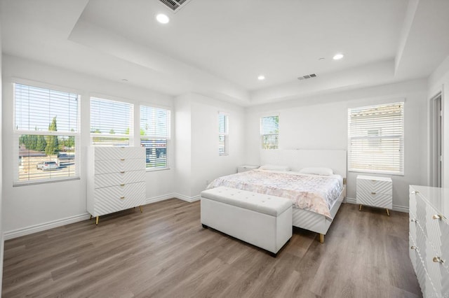 bedroom with visible vents, a tray ceiling, wood finished floors, recessed lighting, and baseboards