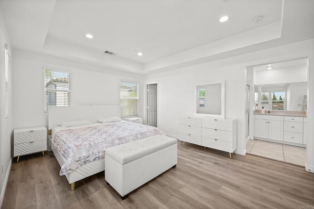 bedroom featuring visible vents, a raised ceiling, and light wood-style floors