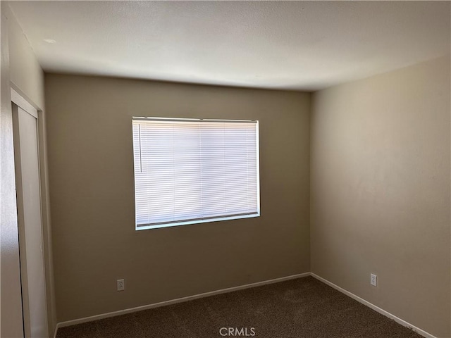 empty room featuring dark carpet and baseboards